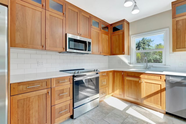 kitchen featuring a sink, light countertops, stainless steel appliances, decorative backsplash, and glass insert cabinets