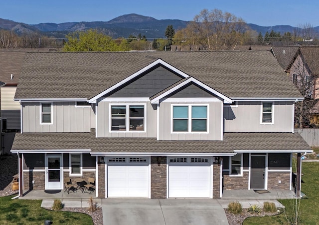 view of front facade with concrete driveway, roof with shingles, a mountain view, and stone siding