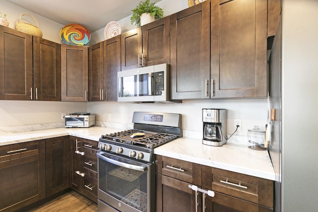 kitchen featuring light stone counters, dark brown cabinetry, and stainless steel appliances