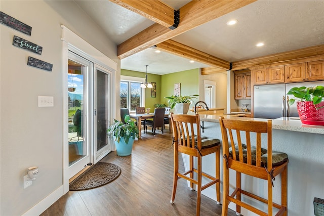 kitchen featuring a breakfast bar, beamed ceiling, recessed lighting, built in fridge, and dark wood finished floors