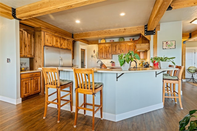 kitchen with brown cabinetry, a kitchen bar, beamed ceiling, a peninsula, and dark wood-type flooring
