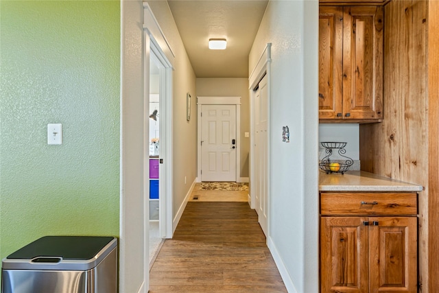 hall with baseboards, a textured wall, and wood finished floors