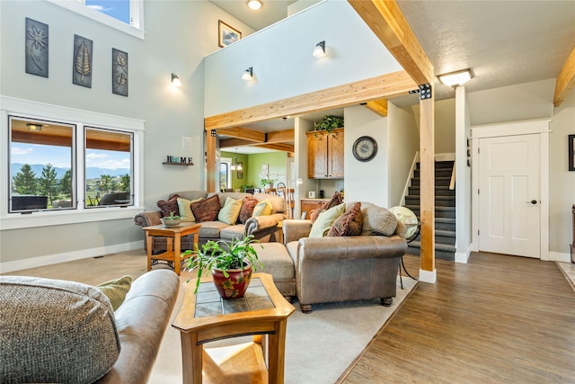 living area featuring baseboards, stairs, light wood finished floors, and beam ceiling