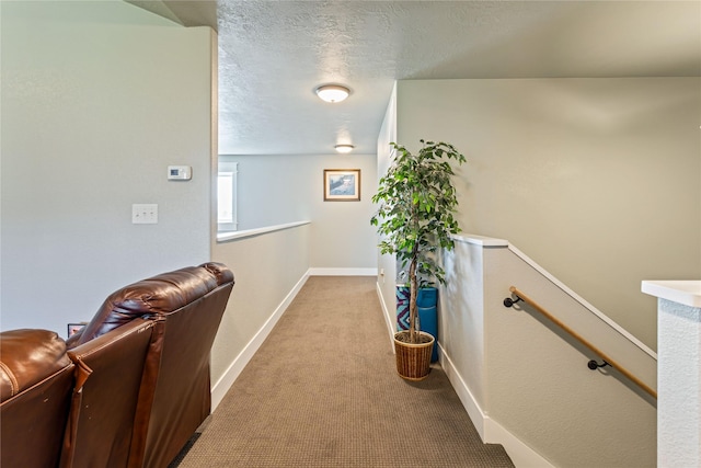 hall featuring a textured ceiling, baseboards, an upstairs landing, and carpet