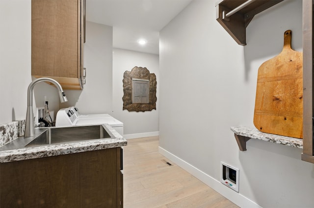 laundry room with baseboards, light wood-type flooring, washing machine and clothes dryer, a sink, and cabinet space