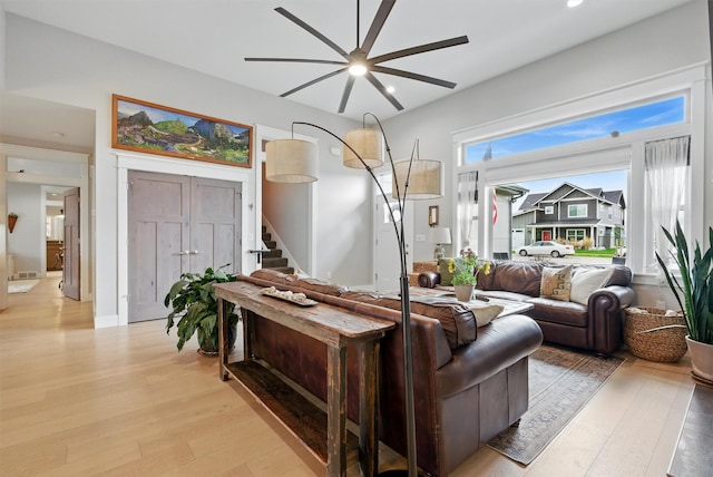 living area with stairs, ceiling fan, and light wood finished floors