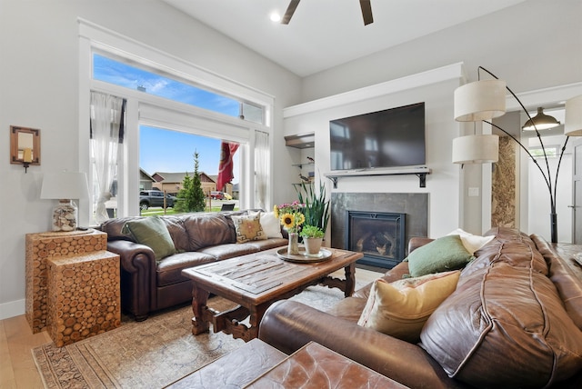 living room with a tiled fireplace, baseboards, and ceiling fan
