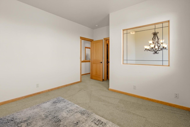 empty room featuring carpet floors, baseboards, and a chandelier