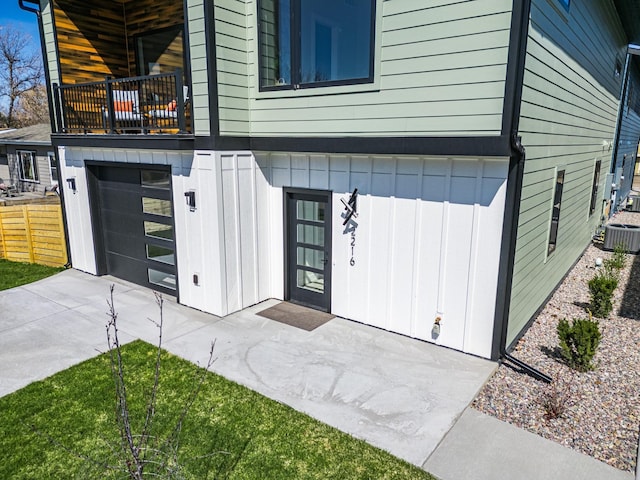 entrance to property featuring central AC, a balcony, board and batten siding, an attached garage, and driveway