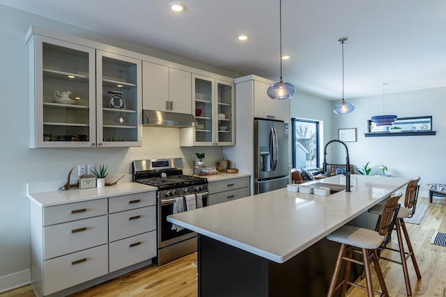 kitchen featuring a kitchen breakfast bar, a center island with sink, under cabinet range hood, light wood finished floors, and stainless steel appliances