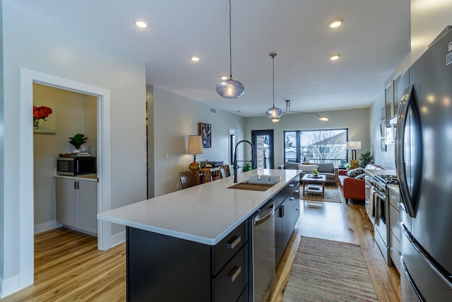 kitchen featuring appliances with stainless steel finishes, a sink, light wood finished floors, light countertops, and open floor plan