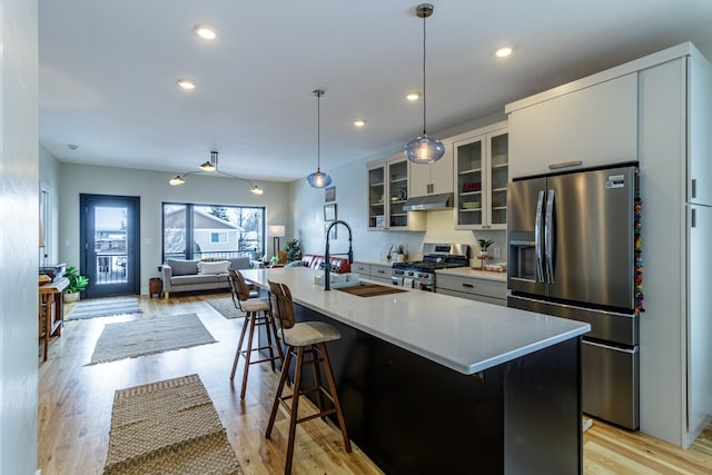 kitchen featuring appliances with stainless steel finishes, a center island with sink, a sink, a breakfast bar, and under cabinet range hood