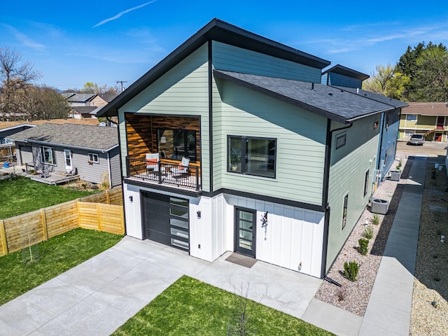 view of front of house with fence, an attached garage, board and batten siding, concrete driveway, and a balcony