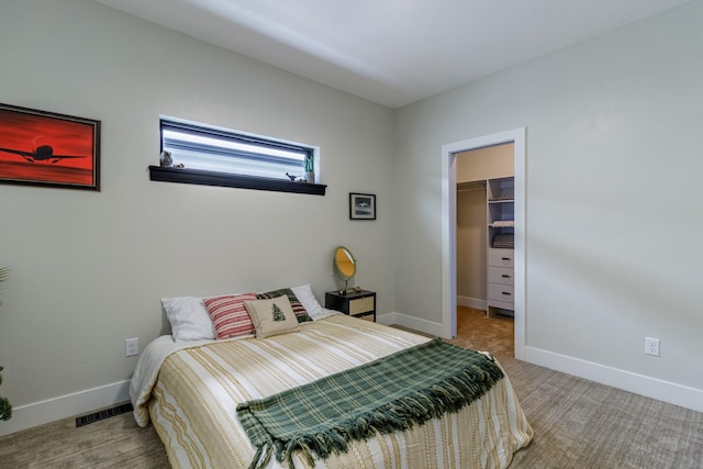 carpeted bedroom with a walk in closet, baseboards, and visible vents