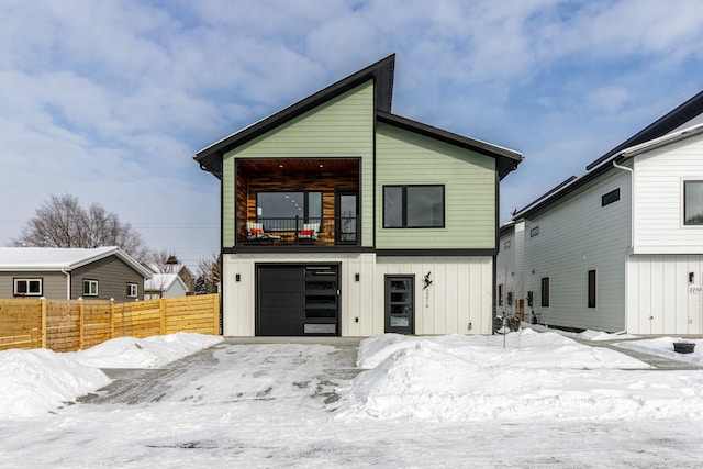 view of front of property with an attached garage, board and batten siding, fence, and a balcony