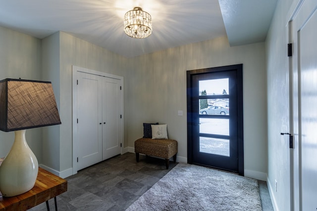 foyer with baseboards, a chandelier, and stone finish floor
