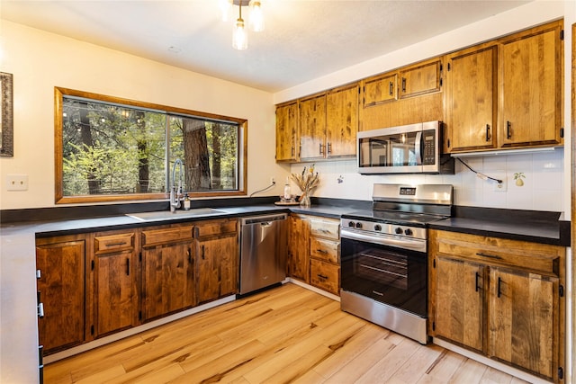 kitchen with appliances with stainless steel finishes, dark countertops, brown cabinets, a sink, and light wood-style floors