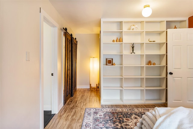 unfurnished bedroom featuring baseboards, light wood finished floors, and a barn door