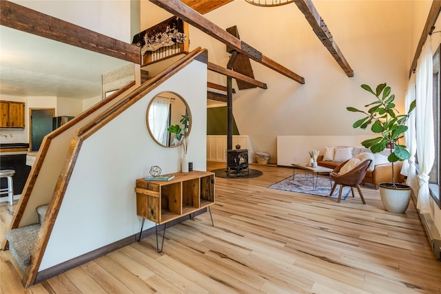 interior space featuring a wood stove, stairs, light wood finished floors, and beamed ceiling