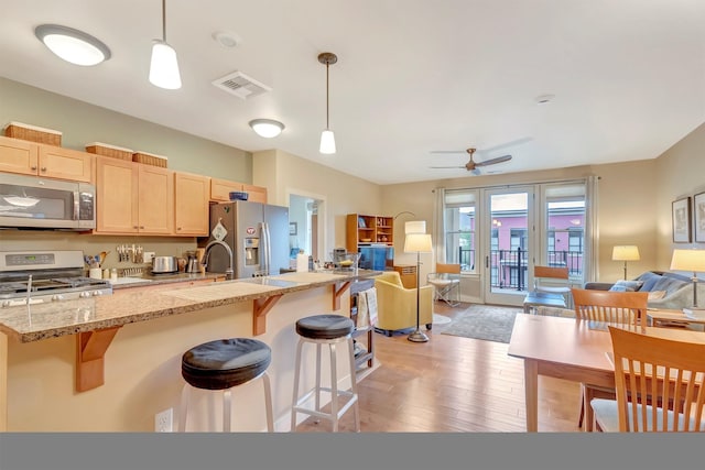 kitchen with light brown cabinetry, light wood-style floors, stainless steel appliances, open floor plan, and a kitchen bar
