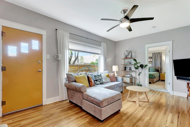 living room featuring baseboards, a ceiling fan, and light wood-style flooring