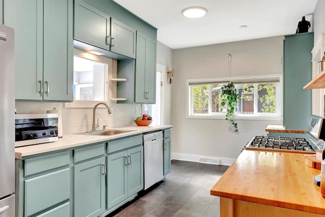 kitchen featuring open shelves, appliances with stainless steel finishes, a sink, baseboards, and visible vents