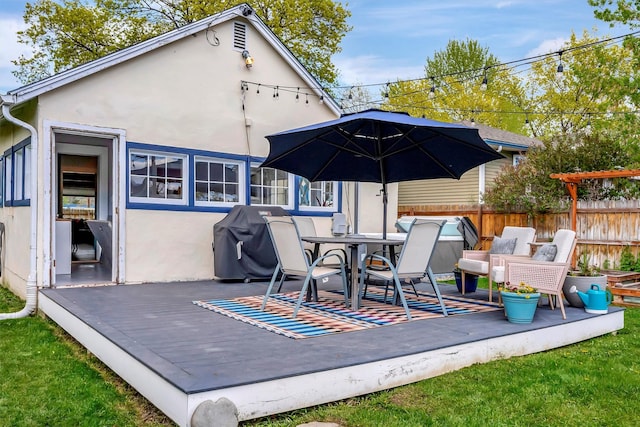 rear view of property featuring stucco siding, outdoor dining area, a wooden deck, and fence