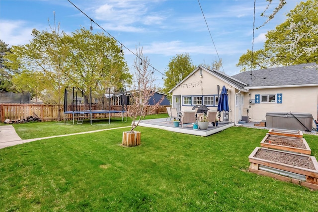 back of property featuring a fenced backyard, a trampoline, stucco siding, and a hot tub