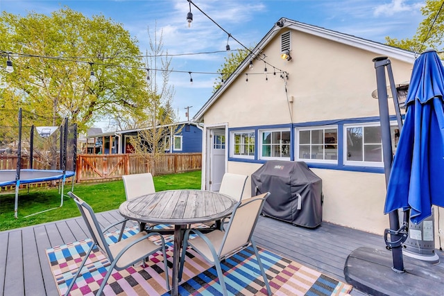 wooden deck with grilling area, a trampoline, fence, a yard, and outdoor dining space