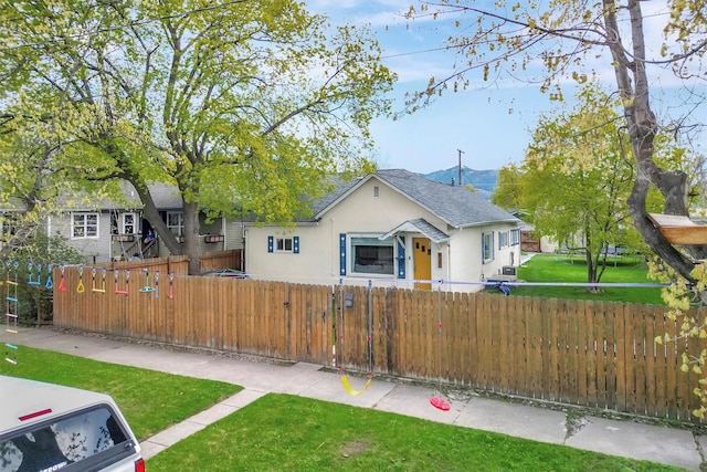 view of front of home with a fenced front yard, a front lawn, roof with shingles, and stucco siding