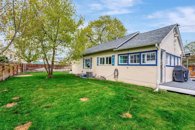 back of house with central AC, a fenced backyard, roof with shingles, stucco siding, and a lawn