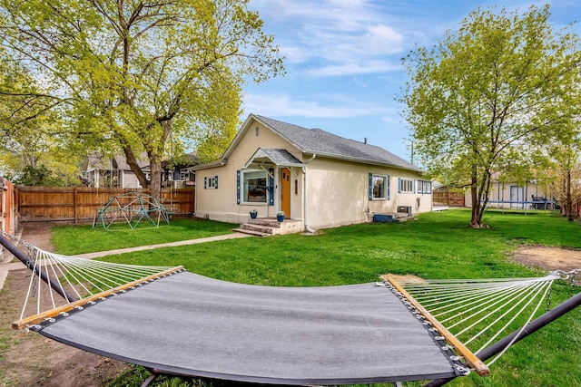 rear view of house with a trampoline, stucco siding, a fenced backyard, a playground, and a lawn