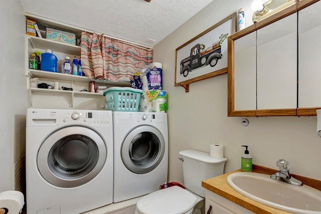washroom with a sink, laundry area, a textured ceiling, and washing machine and clothes dryer