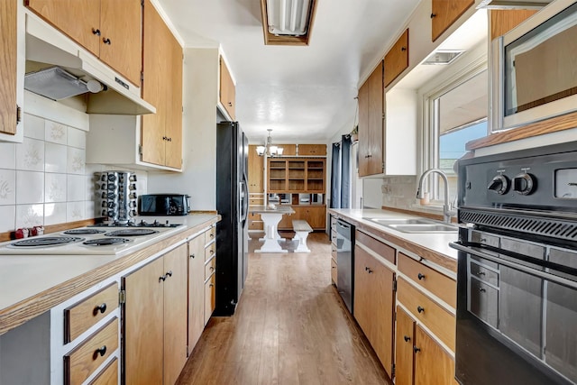 kitchen with a sink, light countertops, a chandelier, under cabinet range hood, and black appliances