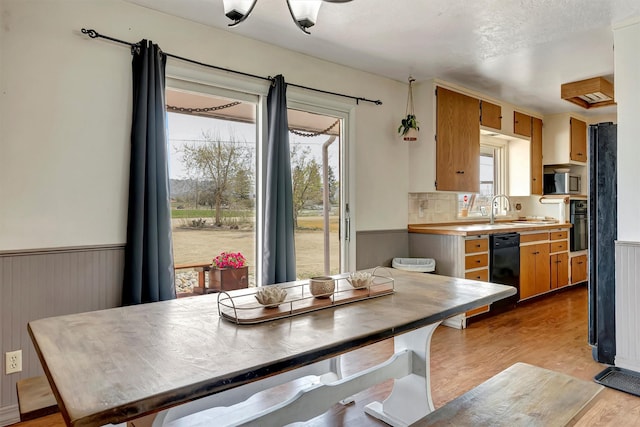 kitchen featuring wainscoting, light countertops, a sink, light wood-style flooring, and black appliances