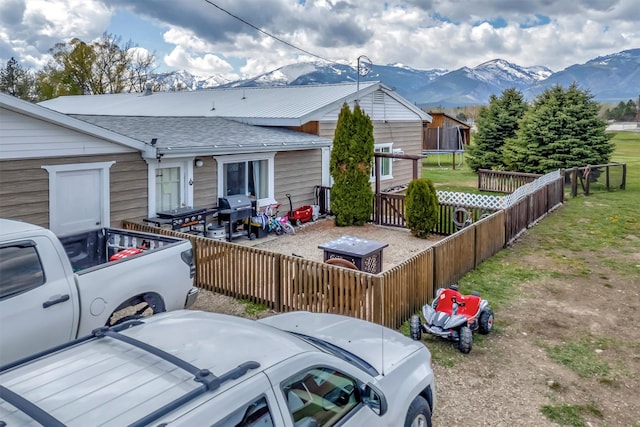 view of home's exterior with a fenced backyard, a mountain view, a shingled roof, and a trampoline