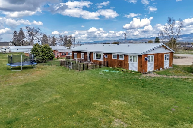 rear view of property featuring a lawn, a trampoline, and fence