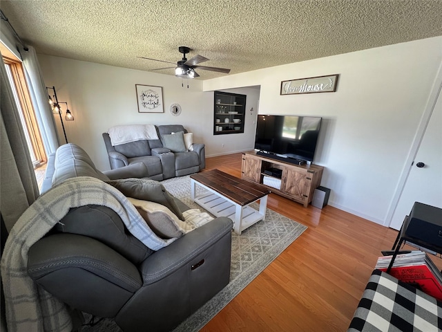living area featuring baseboards, a ceiling fan, a textured ceiling, and wood finished floors