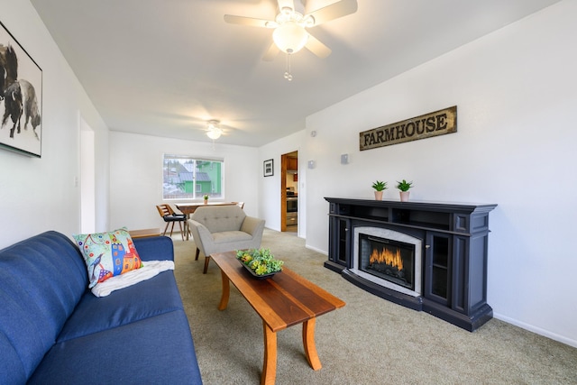 carpeted living area featuring baseboards, a ceiling fan, and a warm lit fireplace