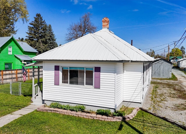 view of side of property with a lawn, fence, a chimney, and metal roof