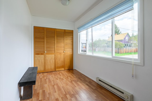 unfurnished bedroom featuring a closet, baseboards, baseboard heating, and light wood-type flooring