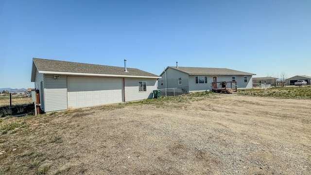 rear view of property with a garage, fence, an outdoor structure, and a wooden deck
