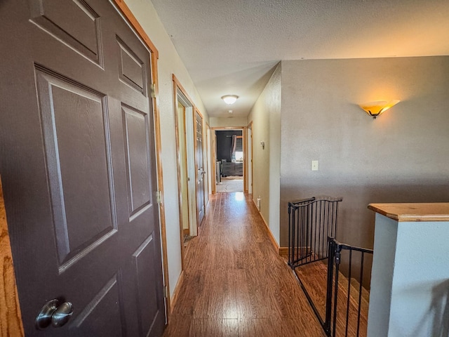 hall featuring baseboards, a textured ceiling, wood finished floors, and an upstairs landing