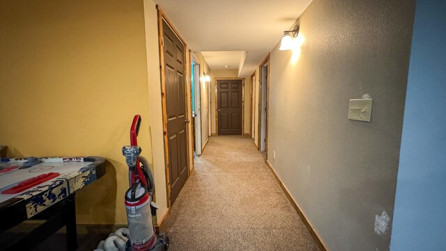 hallway with baseboards and light colored carpet
