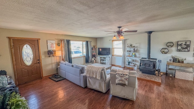 living area featuring a wood stove, a textured ceiling, a ceiling fan, and wood finished floors