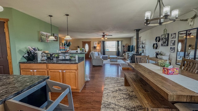 kitchen featuring brown cabinetry, open floor plan, dark wood-type flooring, ceiling fan with notable chandelier, and hanging light fixtures