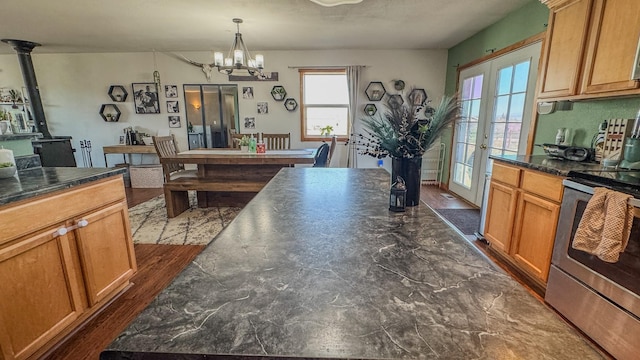 kitchen featuring dark countertops, an inviting chandelier, a wood stove, brown cabinetry, and stainless steel electric stove
