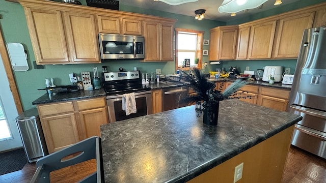 kitchen with brown cabinetry, dark wood-style flooring, a center island, dark stone counters, and stainless steel appliances