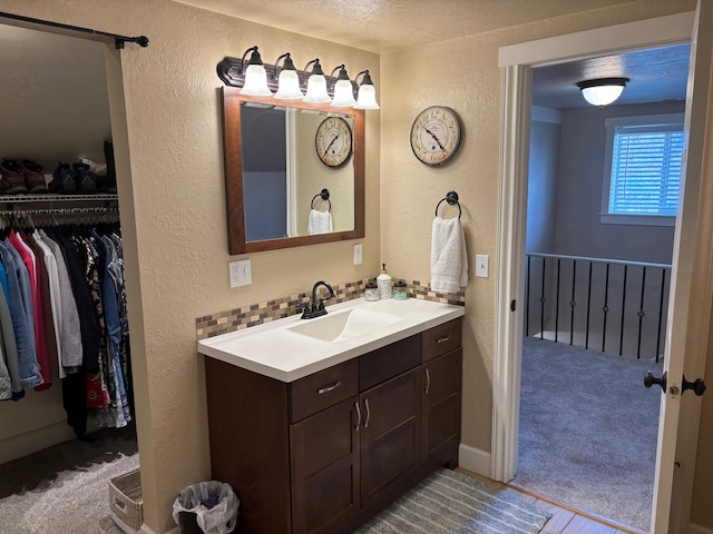 bathroom with vanity, a textured ceiling, a textured wall, and a spacious closet