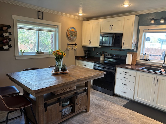 kitchen featuring black microwave, crown molding, electric range oven, a sink, and white cabinets